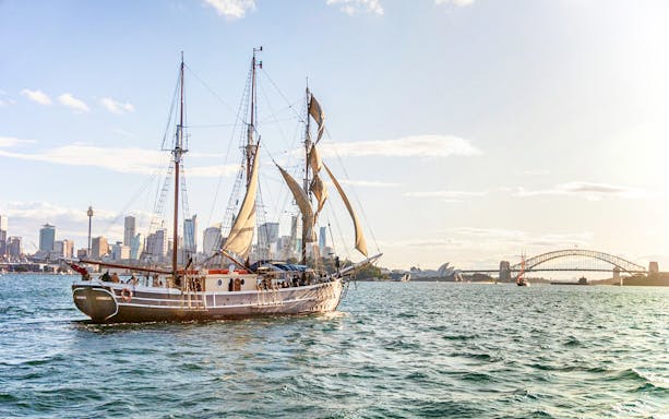 Tall ship sailing in Sydney Harbour with Harbour Bridge in the background.