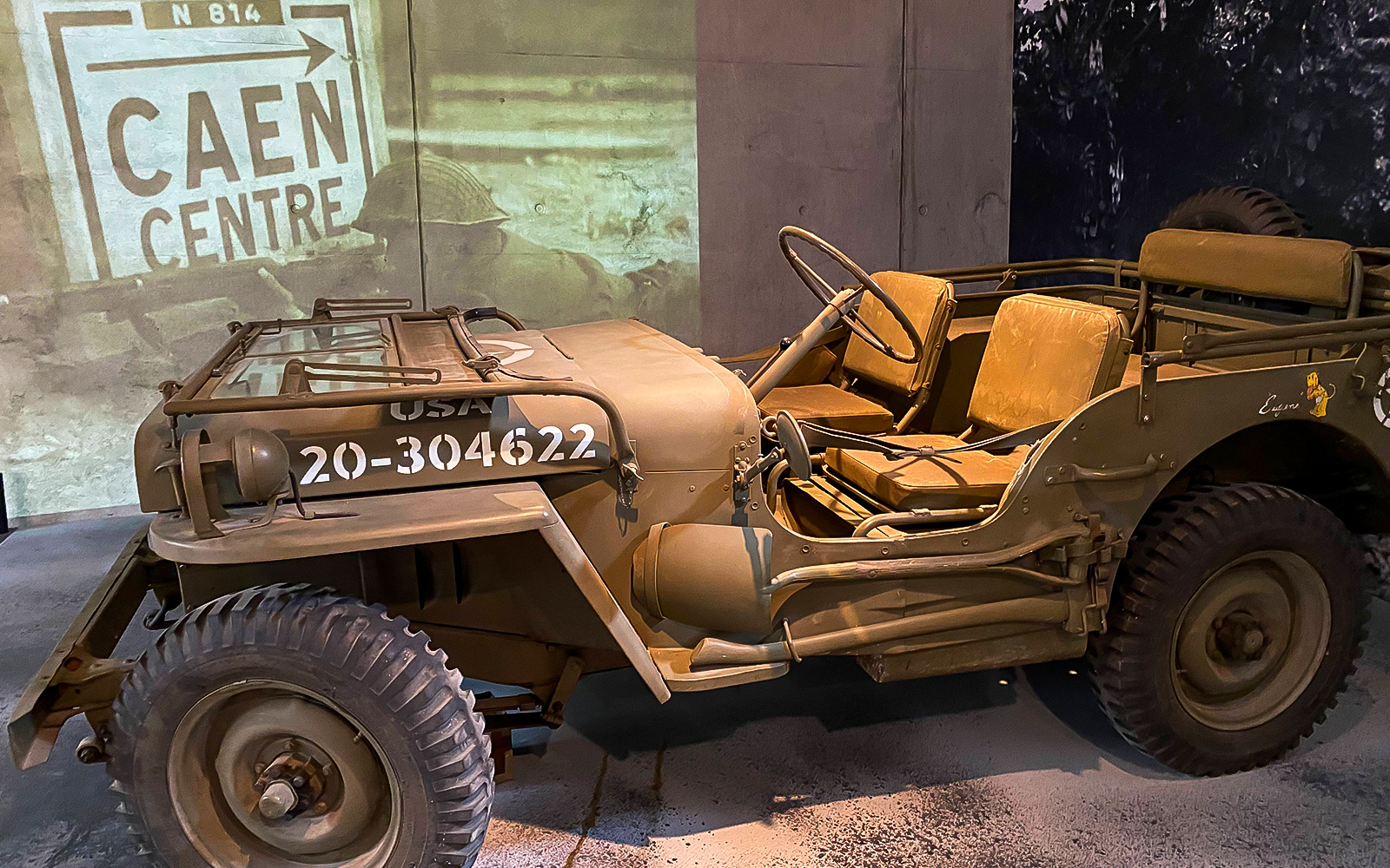 World War II military jeep displayed at D-Day museum in Normandy, with Caen Centre sign in background.