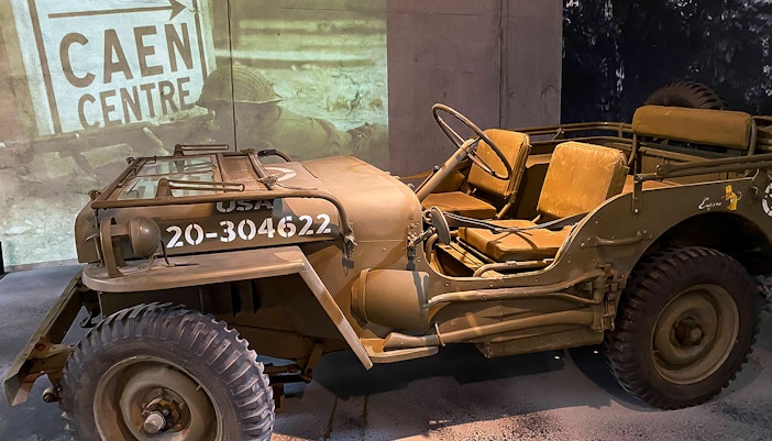 World War II military jeep displayed at D-Day museum in Normandy, with Caen Centre sign in background.