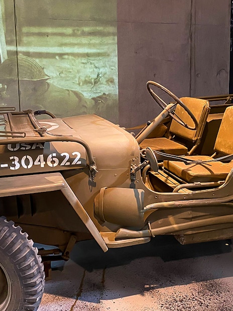 World War II military jeep displayed at D-Day museum in Normandy, with Caen Centre sign in background.