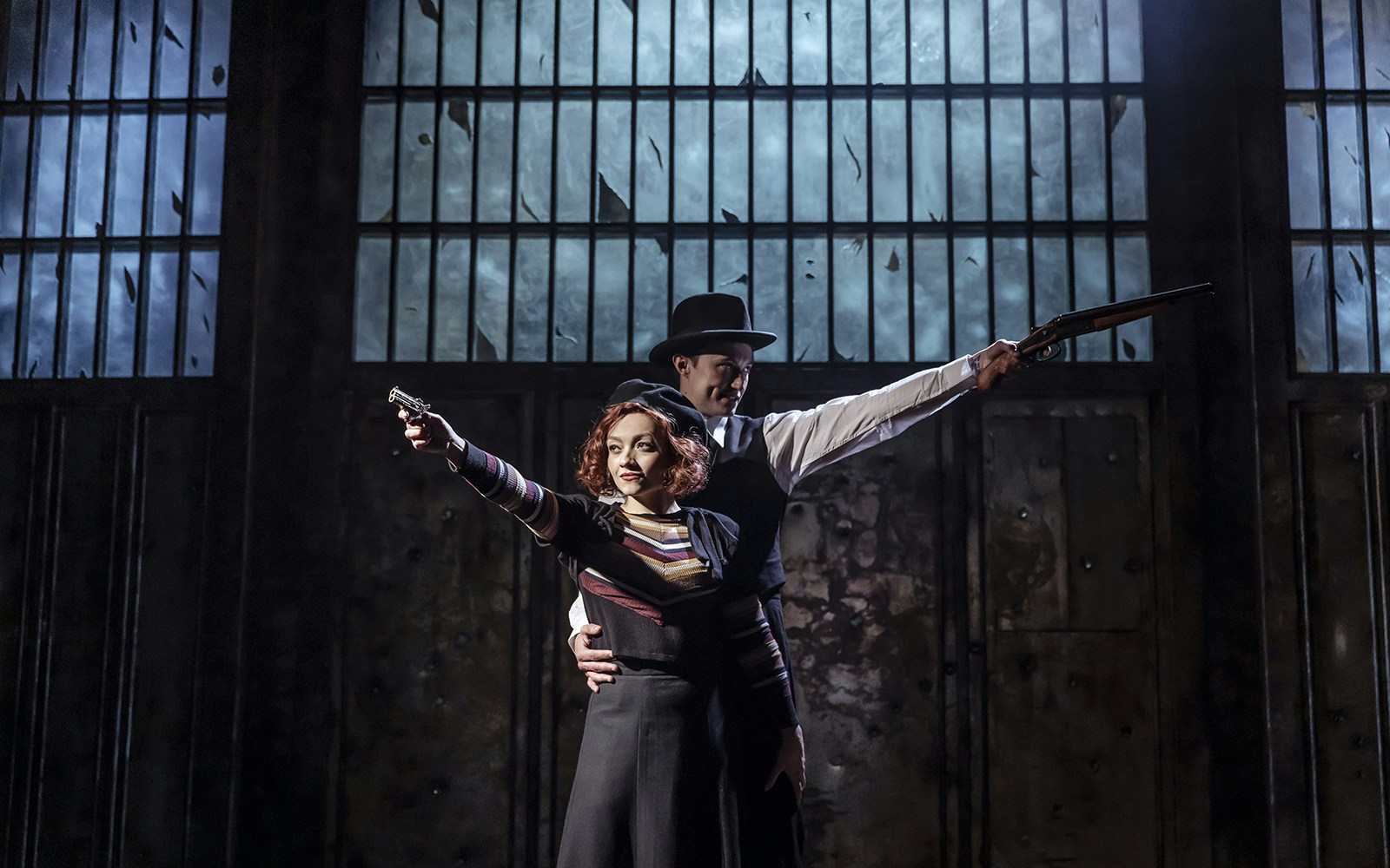 Bonnie and Clyde actors posing with guns in a dramatic stage setting.