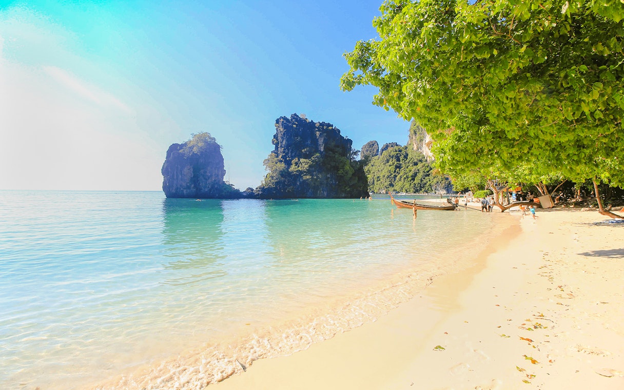 Beach in Ko Hong with clear water, limestone cliffs, and longtail boats along the shore.