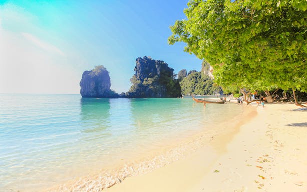 Beach in Ko Hong with clear water, limestone cliffs, and longtail boats along the shore.