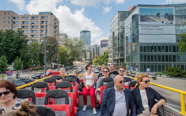 Open-top bus tour with passengers in Warsaw city center.