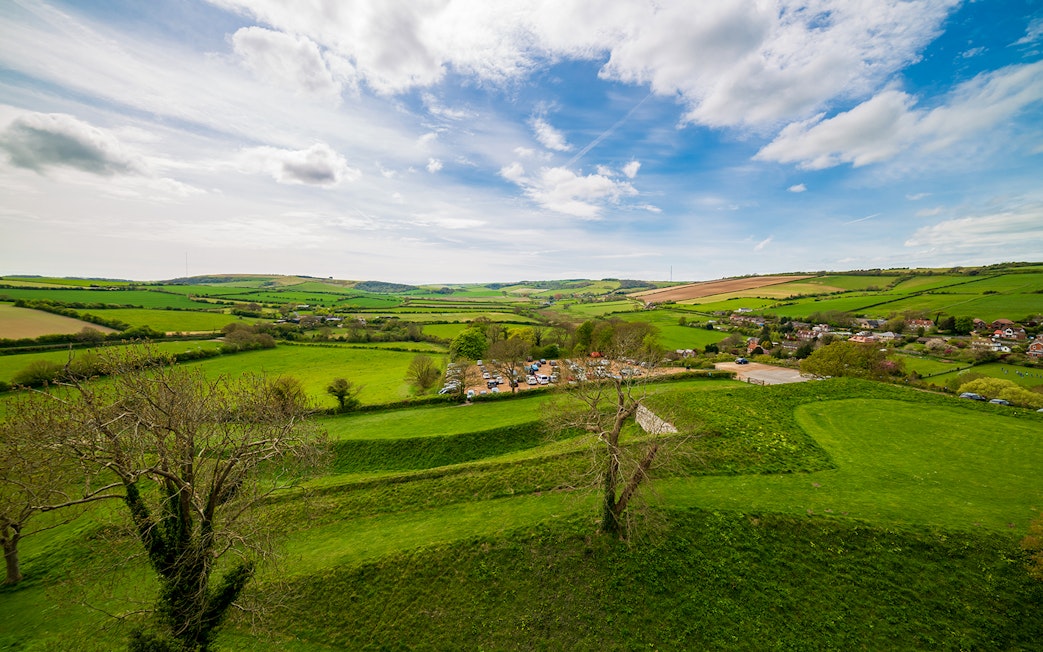 Carisbrooke Castle grounds with lush green fields and distant village view.