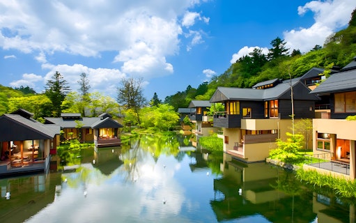 Karuizawa Hoshino Resorts area with modern lodges by a tranquil pond, surrounded by lush greenery.