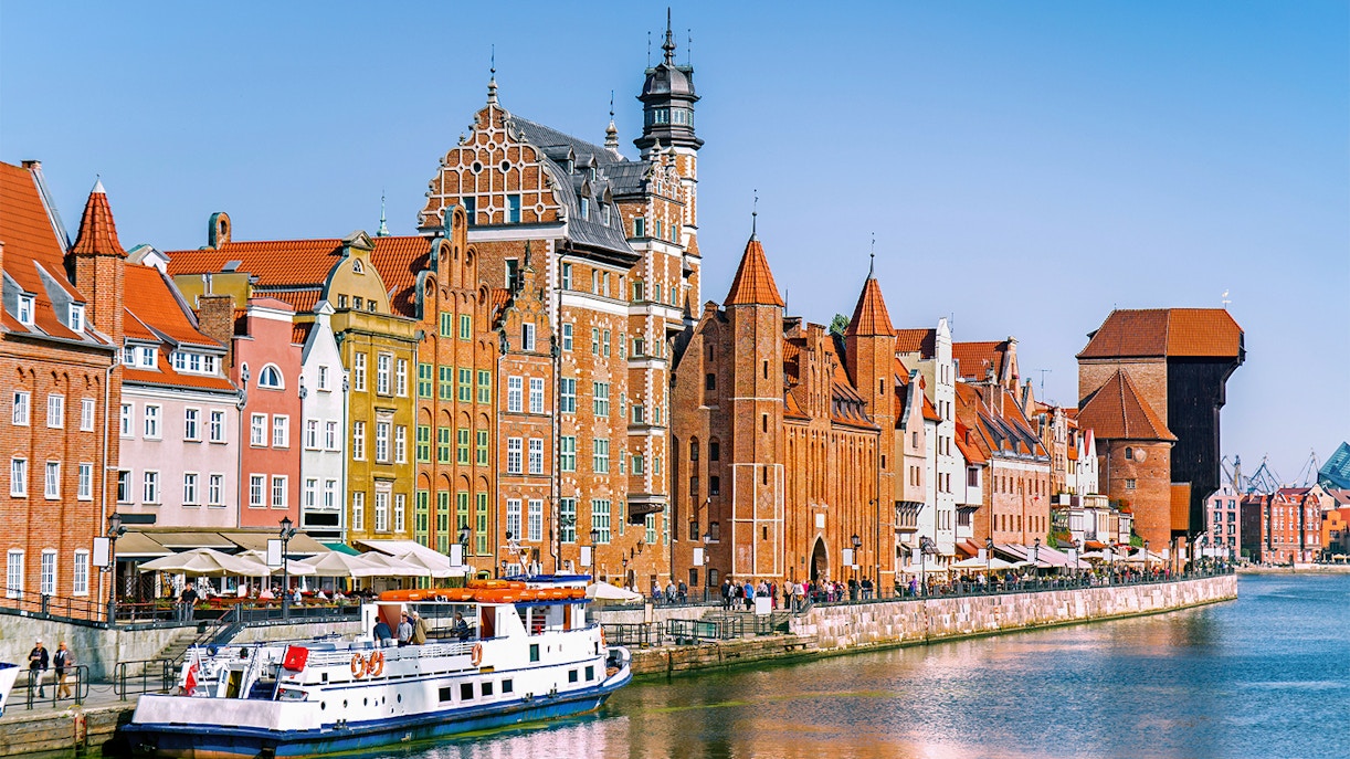 Gdansk waterfront with historic buildings and a cruise boat on the Motlawa River.