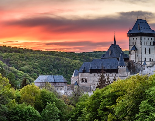 Karlštejn Castle surrounded by lush forest at sunset, showcasing Gothic architecture.