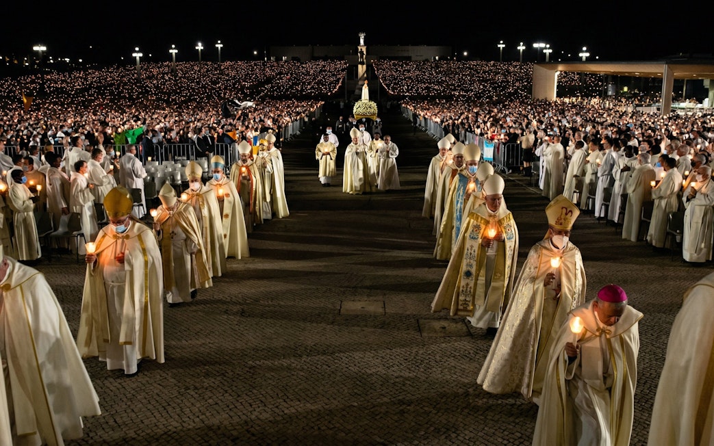 Candlelight procession during Fatima Night Pilgrimage Tour with clergy and large crowd.