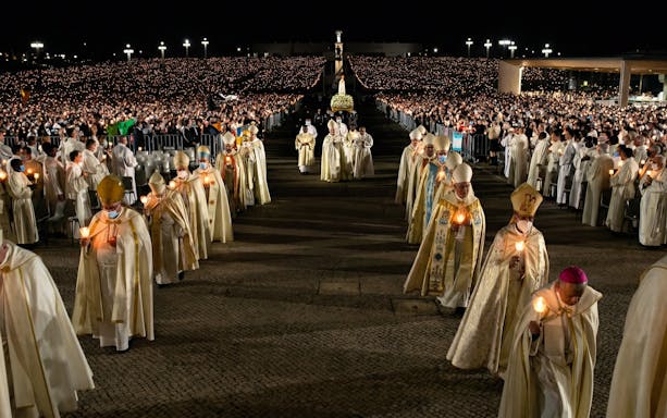 Candlelight procession during Fatima Night Pilgrimage Tour with clergy and large crowd.