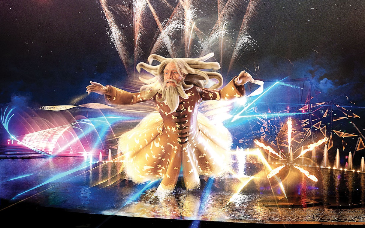 Futuroscope night show with illuminated wizard figure and fireworks display.