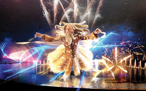 Futuroscope night show with illuminated wizard figure and fireworks display.