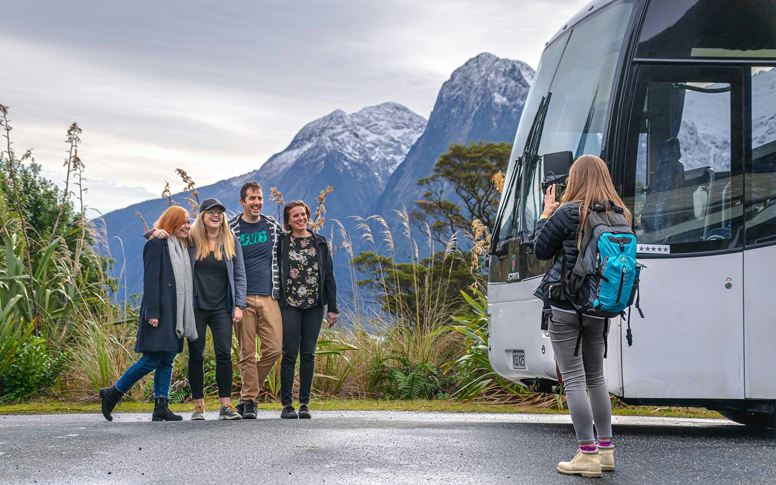 Group of passengers posing for a photo beside a coach with mountains in the background during a trip from Edinburgh to Loch Ness.