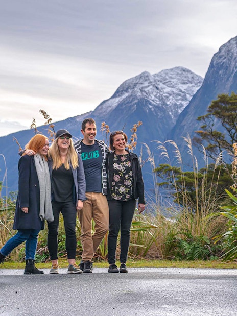 Group of passengers posing for a photo beside a coach with mountains in the background during a trip from Edinburgh to Loch Ness.