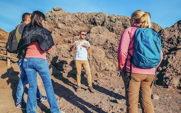 Tourists listening to a volcanologist guide during a hike on Mount Vesuvius.