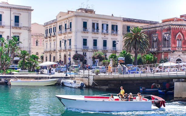 Boat tour passing historic buildings on Ortigia Island, Sicily.