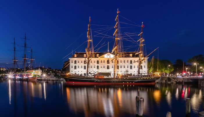 Maritime Museum Amsterdam with historic ship replica in harbor.