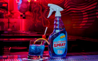 Drinks at Datamosh, Omega Mart with a blue cocktail and spray bottle in a neon-lit setting.