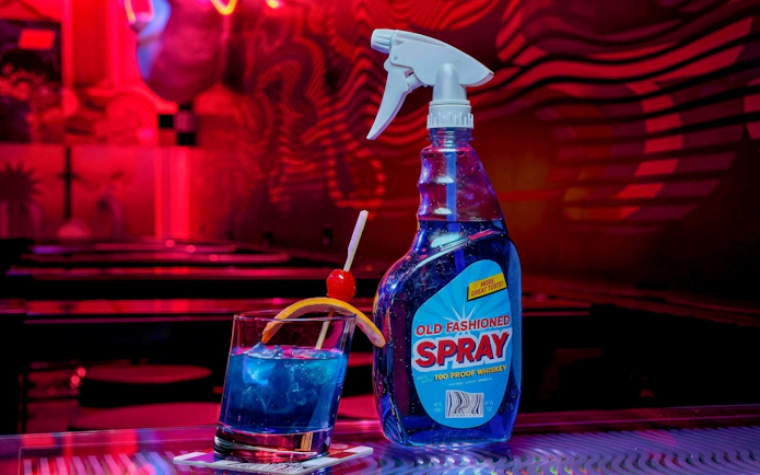 Drinks at Datamosh, Omega Mart with a blue cocktail and spray bottle in a neon-lit setting.