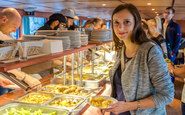 Guests serving food at buffet on evening dinner cruise with live music.