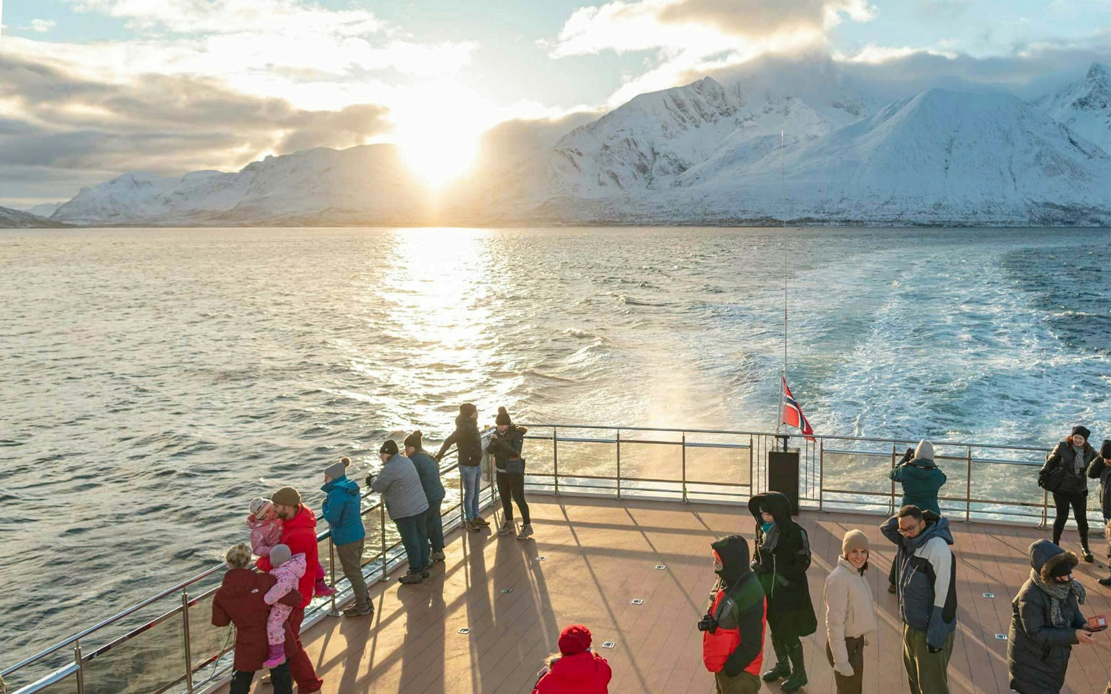 Tourists on a hybrid-electric boat in Tromso, Norway, with snowy mountains and sunset in the background.