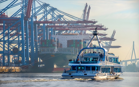 Hamburg harbor cruise ship passing container terminal cranes.