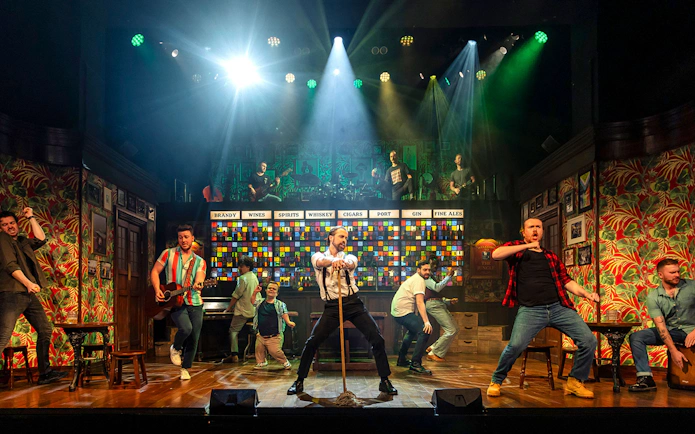 Performers on stage during The Choir of Man show, featuring music and dance in a pub setting.