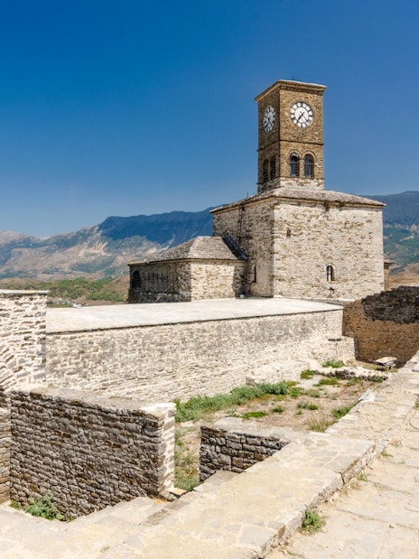 Clock tower at Gjirokaster Castle with mountain backdrop.