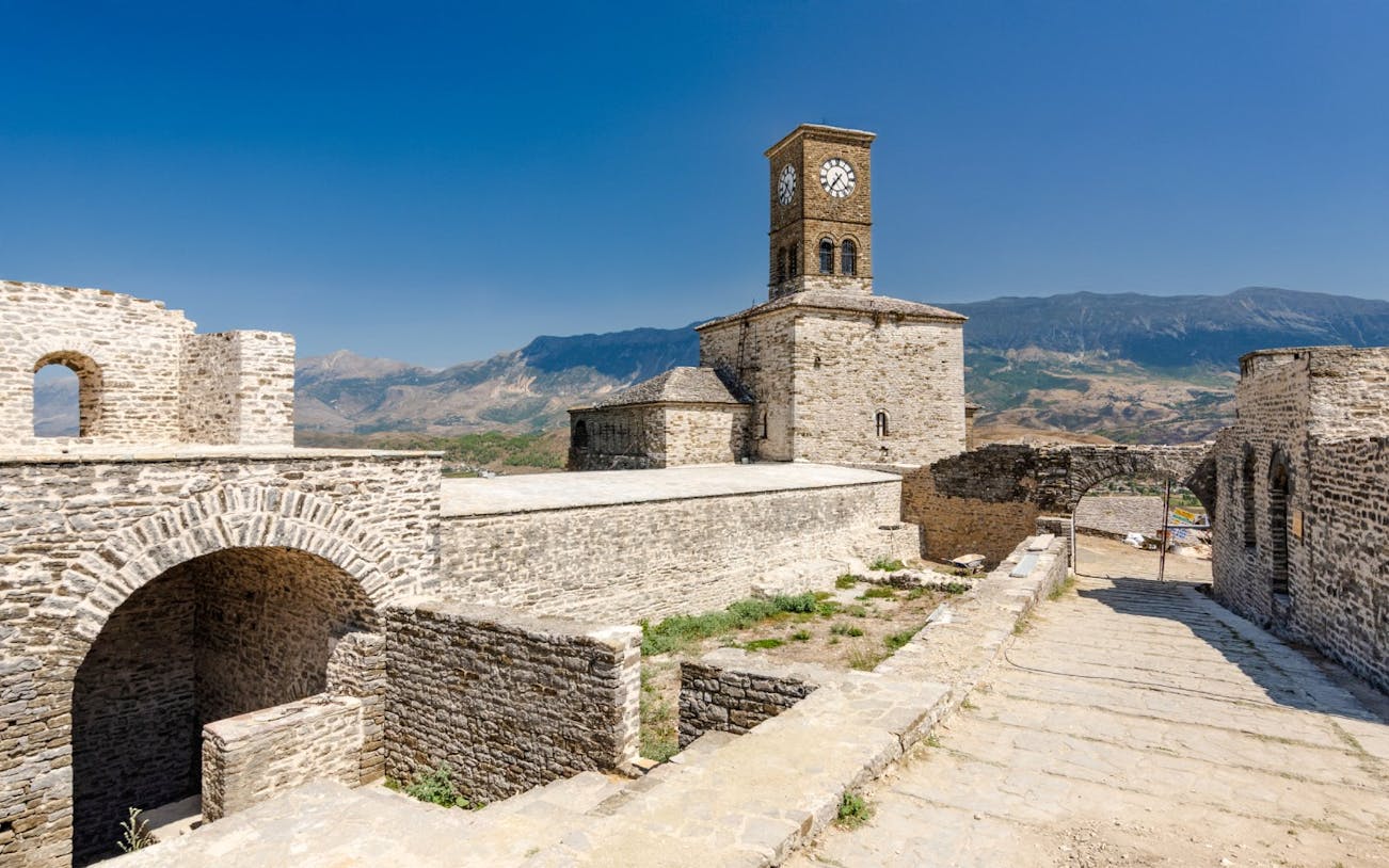Clock tower at Gjirokaster Castle with mountain backdrop.