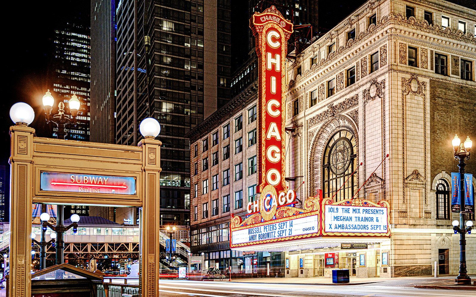 Chicago Theatre marquee lit up at night with nearby subway entrance.