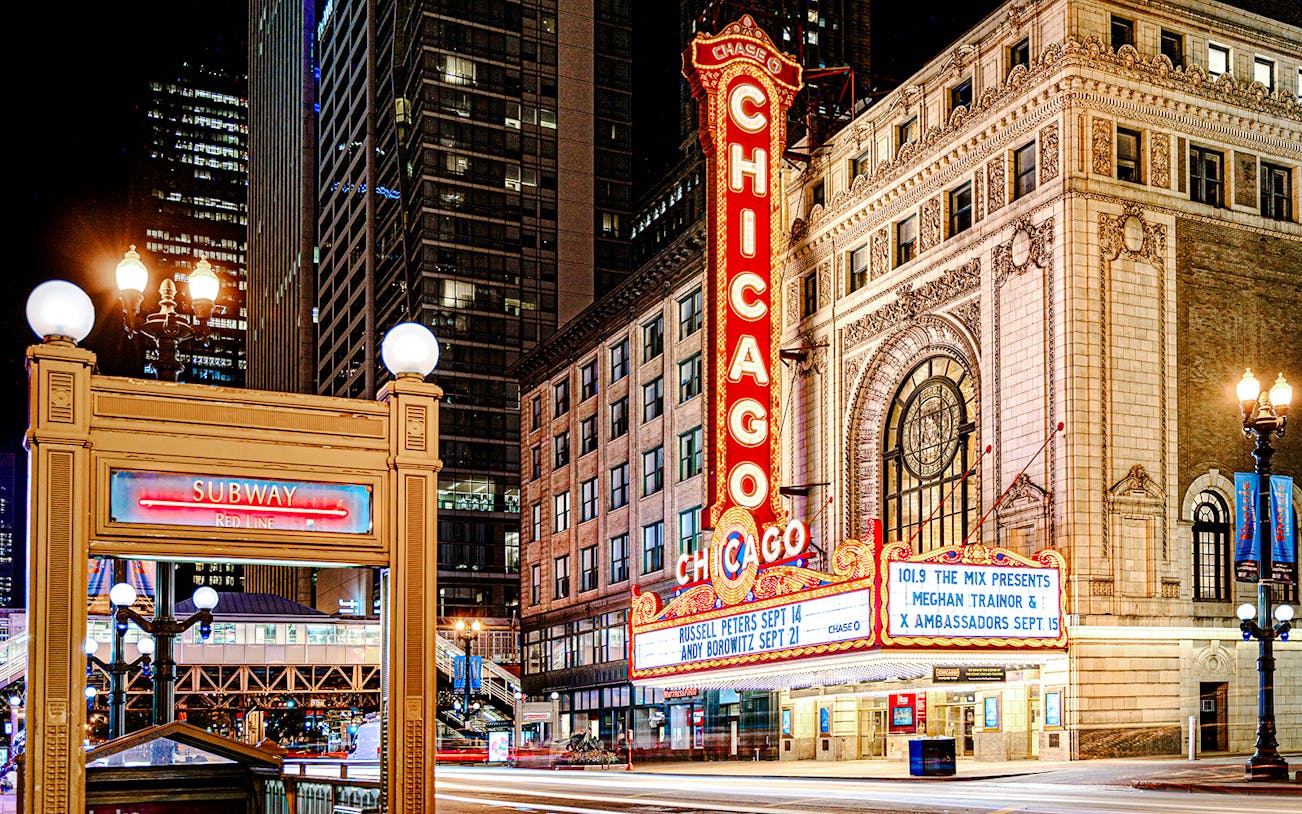 Chicago Theatre marquee lit up at night with nearby subway entrance.