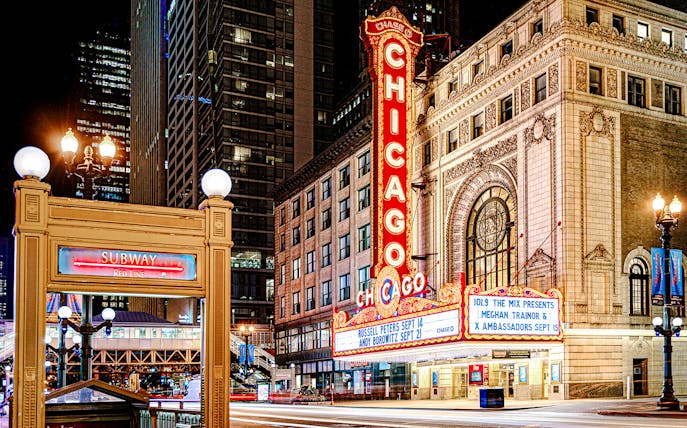 Chicago Theatre marquee lit up at night with nearby subway entrance.