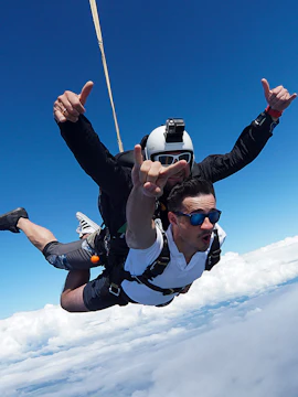 Skydiving tandem over Sydney with clear blue skies and clouds below.