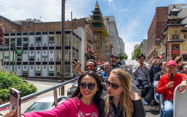 Tourists on an open-top bus during a Hop-On Hop-Off City Day Tour in San Francisco's Chinatown.