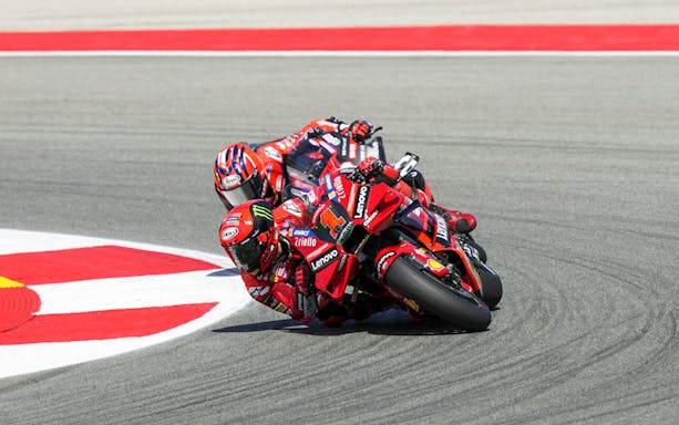 Motorcyclists racing at Petronas Grand Prix of Malaysia 2023 on a sharp track curve.