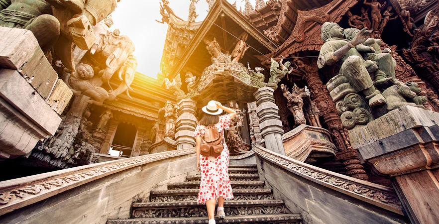 Visitor ascending steps at the intricately carved Sanctuary of Truth in Pattaya, Thailand.