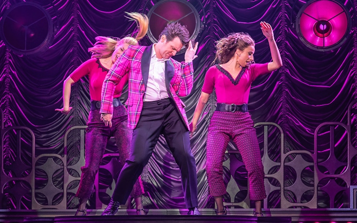 Performers dancing energetically on stage in a vibrant pink setting.
