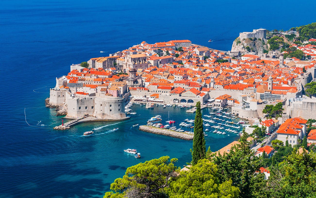 Dubrovnik's Old Town and harbor viewed from above, featuring boats and historic architecture.
