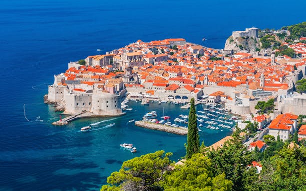 Dubrovnik's Old Town and harbor viewed from above, featuring boats and historic architecture.