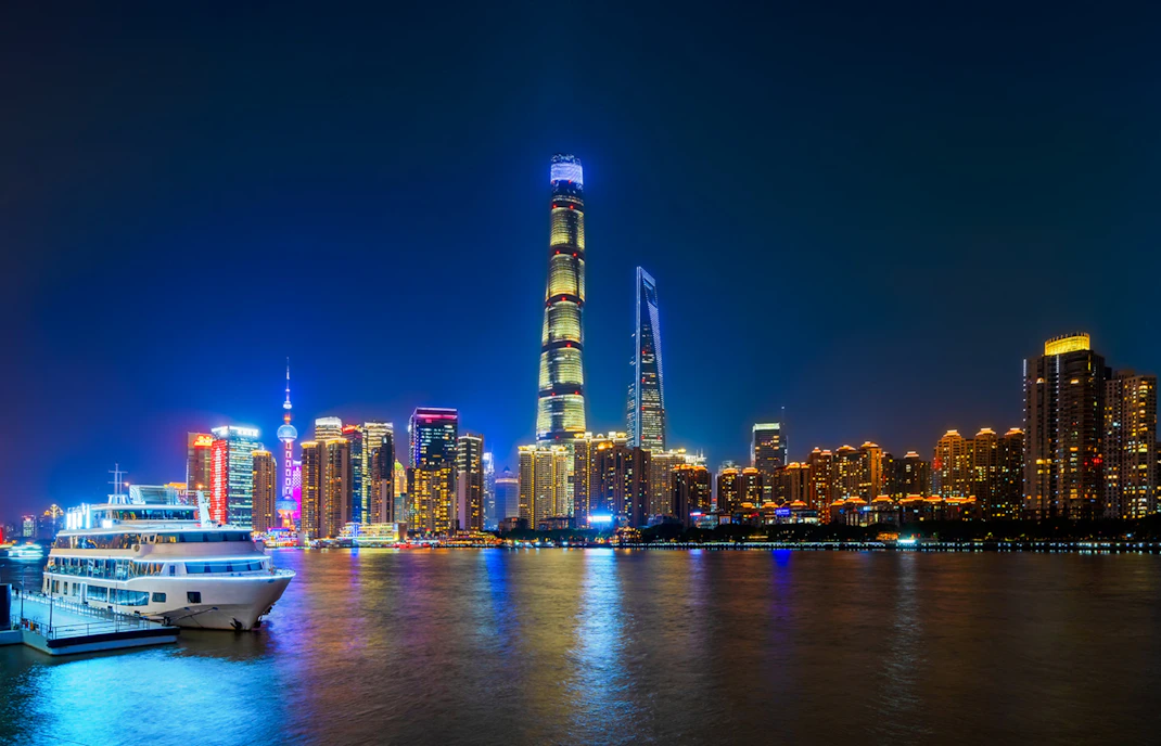 Shanghai skyline at night with skyscrapers, Huangpu River, and boat at Shiliupu Tourist Wharf.