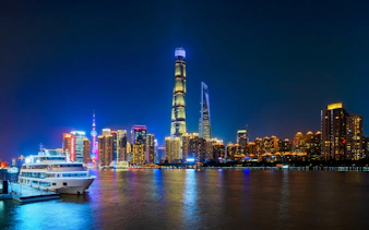 Shanghai skyline at night with skyscrapers, Huangpu River, and boat at Shiliupu Tourist Wharf.