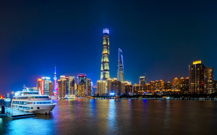 Shanghai skyline at night with skyscrapers, Huangpu River, and boat at Shiliupu Tourist Wharf.
