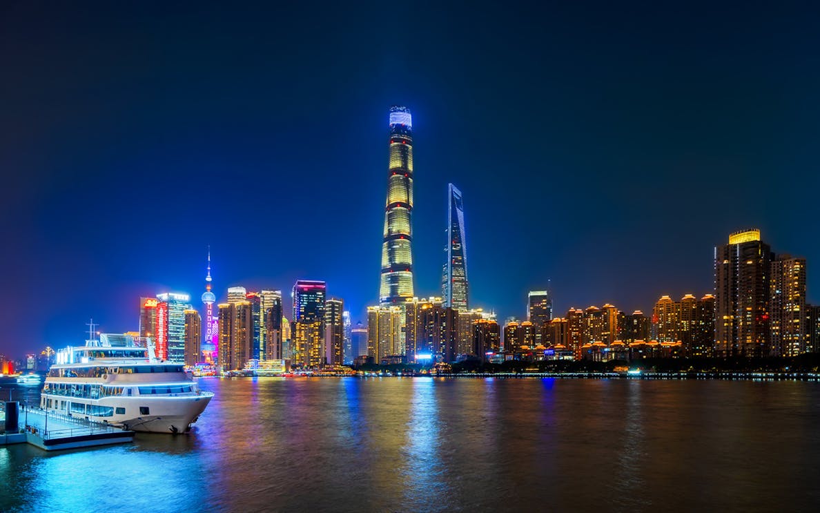Shanghai skyline at night with skyscrapers, Huangpu River, and boat at Shiliupu Tourist Wharf.