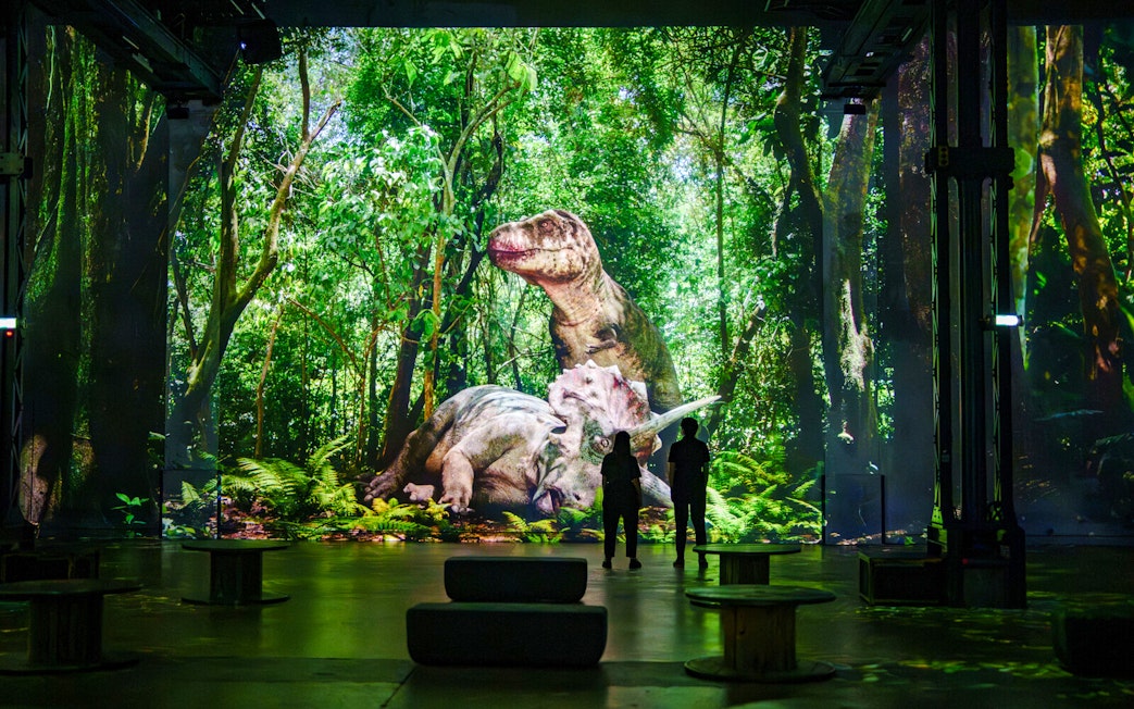 Dinosaurs projected in a lush forest at Prehistoric Planet exhibition, Atelier des Lumières.