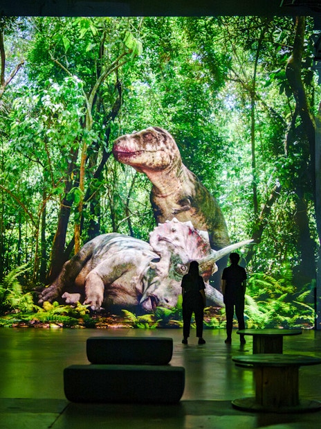 Dinosaurs projected in a lush forest at Prehistoric Planet exhibition, Atelier des Lumières.