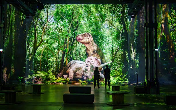 Dinosaurs projected in a lush forest at Prehistoric Planet exhibition, Atelier des Lumières.
