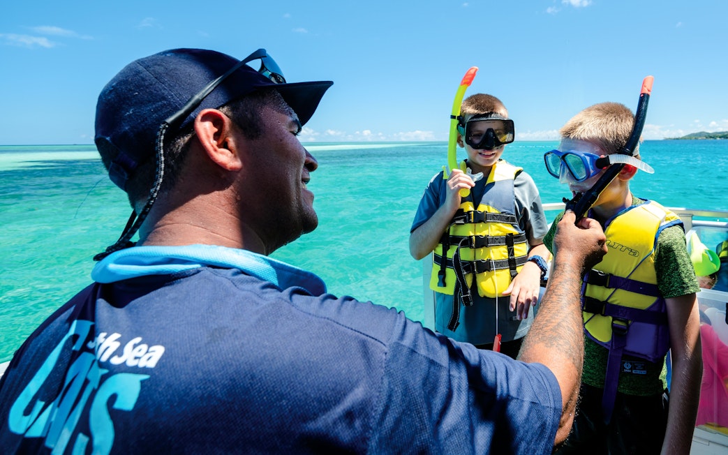 Snorkelling trainer assisting kids with gear on a boat, South Sea Cats, Fiji.