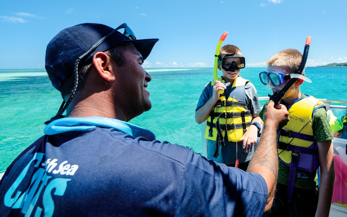 Snorkelling trainer assisting kids with gear on a boat, South Sea Cats, Fiji.