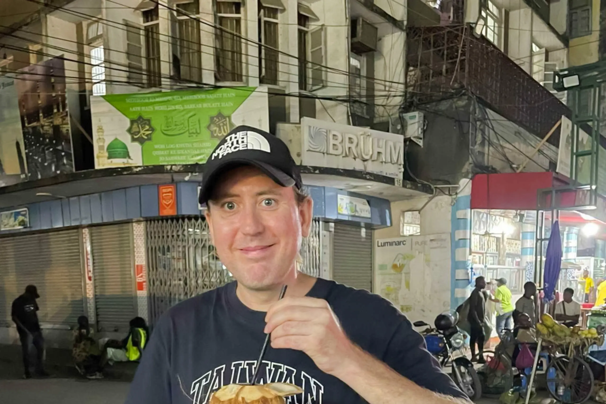 Man enjoying coconut drink on Dar es Salaam street during Old Town walking tour.