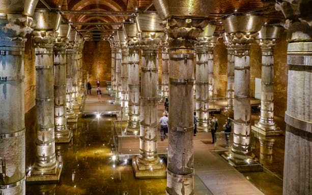 Illuminated columns inside Theodosius Cistern, Istanbul, with visitors exploring.